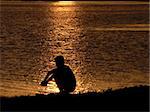 The Sitting boy on background of the reflection sun on water.