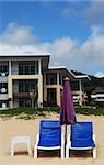 Two blue deck chairs and a table in front of luxury beach front housing