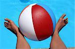 Woman's feet holding beachball by pool