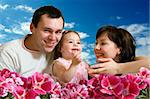 Happy family - mother, father and young cute daughter with flowers and skies as the background