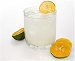 Icy glass of lemonade garnished with a sliced organic lemon over white.