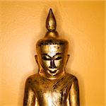 Golden wooden Buddha statue from Burma against yellow wall.