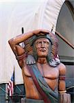 A Wooden Indian near a covered wagon