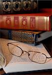 A pair of reading glasses on a book with a stack of old books in the background
