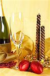 Christmas decoration with champagne bottle, empty glass and candles, over yellow background. Shallow DOF