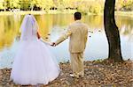 Bride and groom holding hands in autumn park before pond