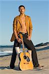 Young man standing with his guitar at the beach