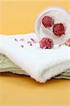 Spa essentials (cream, white towel and flowers) isolated on yellow