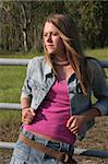 A pretty, country girl leaning on a fence and looking toward the future