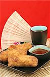 Crispy golden egg rolls served with tea against a red background.  Vertical with room for text.
