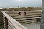 A sign on the boardwalk at the beach, while a storm rolls in over the ocean.