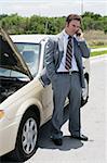 A businessman on the road with a flat tire.  He's calling his next appointment to say he will be late.