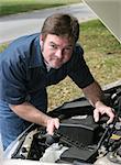 A handsome auto mechanic checking under the hood of a car.  Vertical