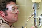 Plumber in safety goggles using a welding torch to solder pipe.