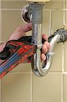 A closeup of a plumbers hands using a pipe wrench to tighten a pipe.