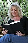 A beautiful mature woman relaxing and reading a book on her porch swing.