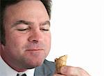 A closeup of a businessman eating an ice cream cone and smiling with his mouth full. Isolated with room for text.
