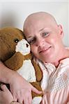 A cancer survivor hugging a teddy bear and smiling.