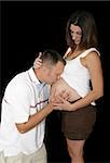 An expectant father kissing his wife's pregnant belly.  Black background.