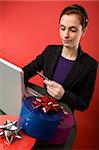 A young female shopping for christmas presents online.  Focus is on the presents with the model and computer blurred.