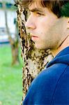 A male standing by a tree thinking