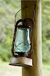 A rusty old oil lamp hangs from a nail in a post.