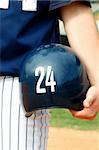 young athlete holds navy blue helmet with the number "24" on it.  His uniform is navy and white.