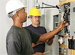 An african american and a caucasian electrician working on a panel.  Actual electricians performing work according to industry safety and code standards.