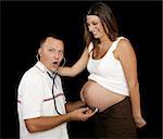 New father listening to his wife's pregnant belly with a stethescope.  Black background