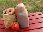 apple cider, an apple and a bag of cinnamon-sugared donuts on a red picnic table