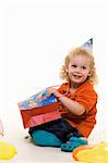 Adorable little three year old boy wearing party hat sitting with balloons with hand in a gift bag