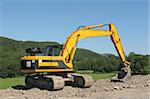 Yellow digger standing idle on a building construction site with rural countryside and a blue sky to the rear.