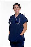 Confident woman healthcare worker wearing dark blue scrubs with stethoscope around shoulders with hands in pockets smiling standing on white