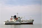 Image shows a white merchant ship floating over calm waters