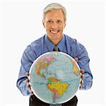 Middle aged Caucasian man holding globe towards viewer.