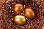 Two chocolate eggs and one gold lay in a nest