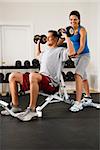 Woman assisting man lifting weights at gym.