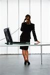 Back view of Caucasian businesswoman standing at computer desk on telephone.