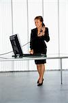 Caucasian businesswoman standing at computer desk on telephone.