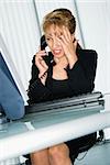 Caucasian businesswoman with hand to head and frustrated expression at computer desk on telephone.