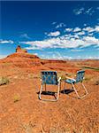 Two outdoor lawn chairs in scenic desert landscape with mesa land formation.