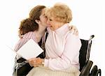 Grandmother reading a greeting card and getting a kiss from her teenaged granddaughter.  Isolated on white.