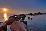 Sunrise in Sardinia with lighthouse and stone pier