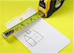 a measuring tape over a drawing of a house on a notepad