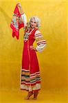 Russian woman in a folk russian dress waves a scarf on yellow background