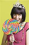 Pretty young woman takes a bite from a large lollipop