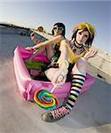 Fisheye shot of girls in brightly colored clothing in a plastic pool on a roof with lollipops