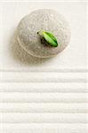 Stone on raked sand with a green leaf on a top. Zen concept
