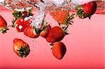 Strawberries falling in red water with splash and bubbles