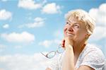The elderly woman smiles and holds in hands glasses on a background of the blue sky